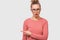 Amazed and excited young woman wearing casual outfit and transparent eyewear, open mouth in panic pointing finger draws your