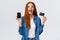 Amazed, happy and surpirsed, cheerful caucasian redhead woman showing credit card and smartphone display, app on mobile