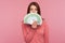 Amazed happy woman with brown hair in pink sweater hiding face behind fan of euro banknotes, interest-free cash withdrawal