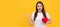 amazed lady in white shirt with heart presenting product on yellow background, copy space, donation. Woman isolated face