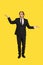 Amazed middle aged businessman in black suit balancing with hands invisible objects isolated on yellow background