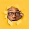 Amazed shocked millennial black male in glasses open mouth looks through hole in yellow paper, square