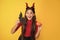 amazed teen girl wearing imp horns holding pumpkin and bat on yellow background, november