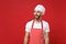 Amazed young bearded male chef cook or baker man in striped apron white t-shirt toque chefs hat posing isolated on red