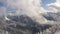 Amazing backward view snowy fir trees in lowlands on cloudy sky background. Glorious winter forest in misty haze in mountain valle