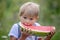 Amazing blond toddler child, boy with pet dog, eating watermelon in garden