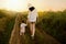 Amazing, charming, adorable view of a pretty mother in a hat and little beautiful daughter walking on a path of a field. Sunset or
