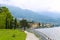 Amazing coastline with banister and grass with trees, Alps mountain in background.