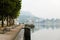 Amazing coastline with benches and trees near sea, buildings and mountain in background.