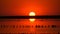 Amazing incredible red sunset with a huge round sun on a salt lake against the backdrop of silhouettes of windmills