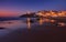 Amazing landscape of the Atlantic ocean coast at dusk. Night view on the village in lights, reflecting on a sandy beach. Portugal.