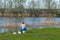 Amazing landscape of pictorial forest with green lawn, trees and pond, near shore of which sits fisherman with fishing rod