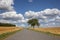 Amazing landscape, rural scene with clouds, tree and empty road summertime, fields of haystack next to the road