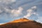 Amazing mountain landscape with cone  rock in golden sunlight under beautiful white clouds. Nature background of rocky mountain