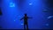 Amazing nature, small boy with raised arms touches the aquarium glass with sharks and fishes in water