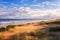 Amazing seascape in soft sunset light with sand dunes, green grass, waves of the sea and blue sky with clouds, travel background