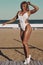 Amazing sexy woman in white swimsuit with perfect sport body posing at the beach. Concept of sport womans body in swimwear