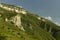 Amazing summer mountain landscape - folded mountain slope with grey layered rocky scree, cliffs under lush green meadows