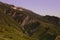 Amazing summer mountain landscape with green folded mountain ridge with rocky cliffs and moon in purple sunlight of sunset.