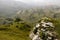 Amazing summer mountain landscape - green folded mountain ridges with terraces with meadow, grey rocky ledge in soft white mist