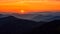 Amazing sunset over mountain range, scenic alpine landscape with dark silhouettes of mountains, fiery yellow sky and sun