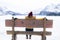 Amazing Swiss Alps viewpoint from wooden bench - happy woman sitting on bench looking snow mountain landscape in front of frozen
