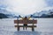 Amazing Swiss Alps viewpoint from wooden bench - happy woman sitting on bench looking snow mountain landscape in front of frozen