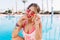 Amazing tanned girl wearing cool pink sunglasses and swimsuit undet shirt playfully posing before swim in pool. Portrait