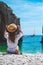 Amazing view from behind of a beautiful brunette sitting by the seaside, stiniva beach in croatia. Holding onto her straw hat