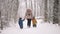 Amazing view of toddler boys and mom walking in winter forest with snowfall background. Babies rejoices first snow