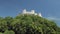Amazing white medieval fortress is on a top of hill covered dense forest, tilt up view