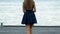 Amazing young woman in a short dress and blue high heels walking on wooden pier by the sea