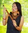 Amazonian exotic woman with facial paint and black dress, holding blowgun, forest background.