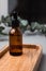 Amber bottle with facial cosmetics on a tray with a branch of eucalyptus on the gray concrete background, facial serum