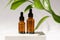 Amber cosmetic bottles with pipette on white podium, product packaging with natural ruscus branch, anti aging serum with peptides