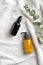 Amber glass bottle with serum, yellow dispenser bottle with body care lotions, eucalyptus leaf on white towel.