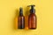 Amber glass cosmetic bottles in droplets of water on yellow background. Spay bottle with sunscreen lotion and pump bottle with