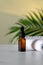 Amber glass dropper bottle and towel on marble table, tropical palm leaf on background. Luxury container mockup for essential oil