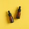 Amber glass dropper bottles with pipette in droplets of water on yellow background. Flat lay, top view. Serum cosmetic packaging,