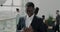 Ambitious African American businessman walking in office center lobby with panoramic windows and checking smartphone