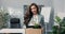 Ambitious beautiful smiling brunette in shirt stands in front of desk in company office in hands holds box with packed