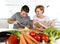 American couple working in domestic kitchen together wife following recipe in cookbook and husband slicing cheese