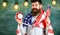 American educational system concept. Man with beard on cheerful face holds flag of USA and clock, chalkboard on