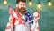 American educational system concept. Man with beard on cheerful face holds flag of USA and clock, chalkboard on