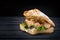 American fast food. Juicy tuna sandwich with cheese, salad and olives on a dark background. Club food.