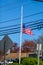 American flag seen at half mast near a street with a blue sky and power lines in the background.