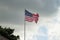 American flag, Stars and Stripes, flying from a flagpole against dark, stormy clouds in the background.