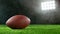 American football ball placed on grass, dark background