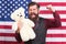 American guy with toy celebrate holiday. American holiday. Man bearded hipster hold teddy bear american flag background