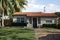 American house with a red tiled roof and a green grass lawn around the facade and an old brick sidewalk in Miami